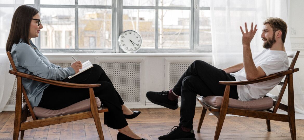 Person in Black Pants and Black Shoes Sitting on Brown Wooden Chair